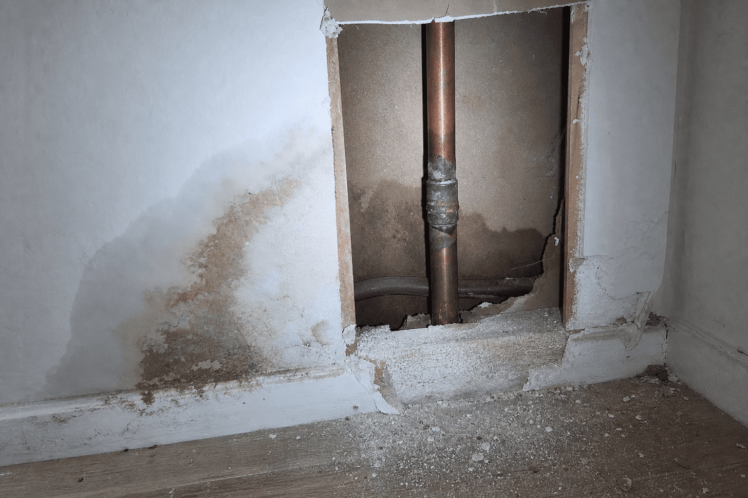 Cloison ouverte, coude d'alimentation en cuivre corrodé et tache d'humidité